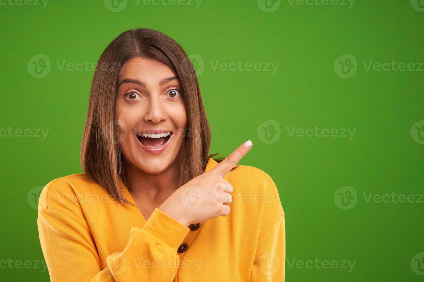 Close up of woman in yellow sweater thinking and pointing over green background photo