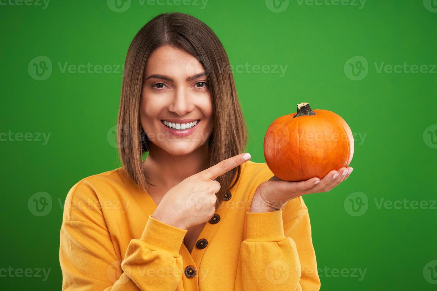 Close up of woman in yellow sweater holding pumpkin over green background photo