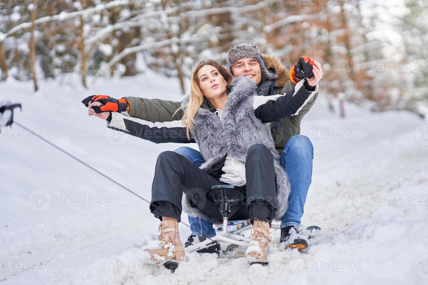 Couple having fun with sledge on snow in winter photo