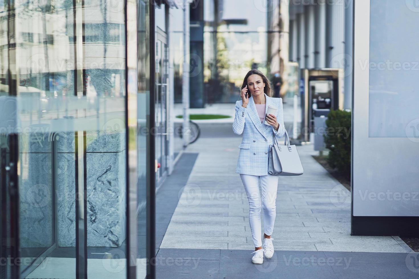 Adult attractive woman with smartphone walking in the city photo