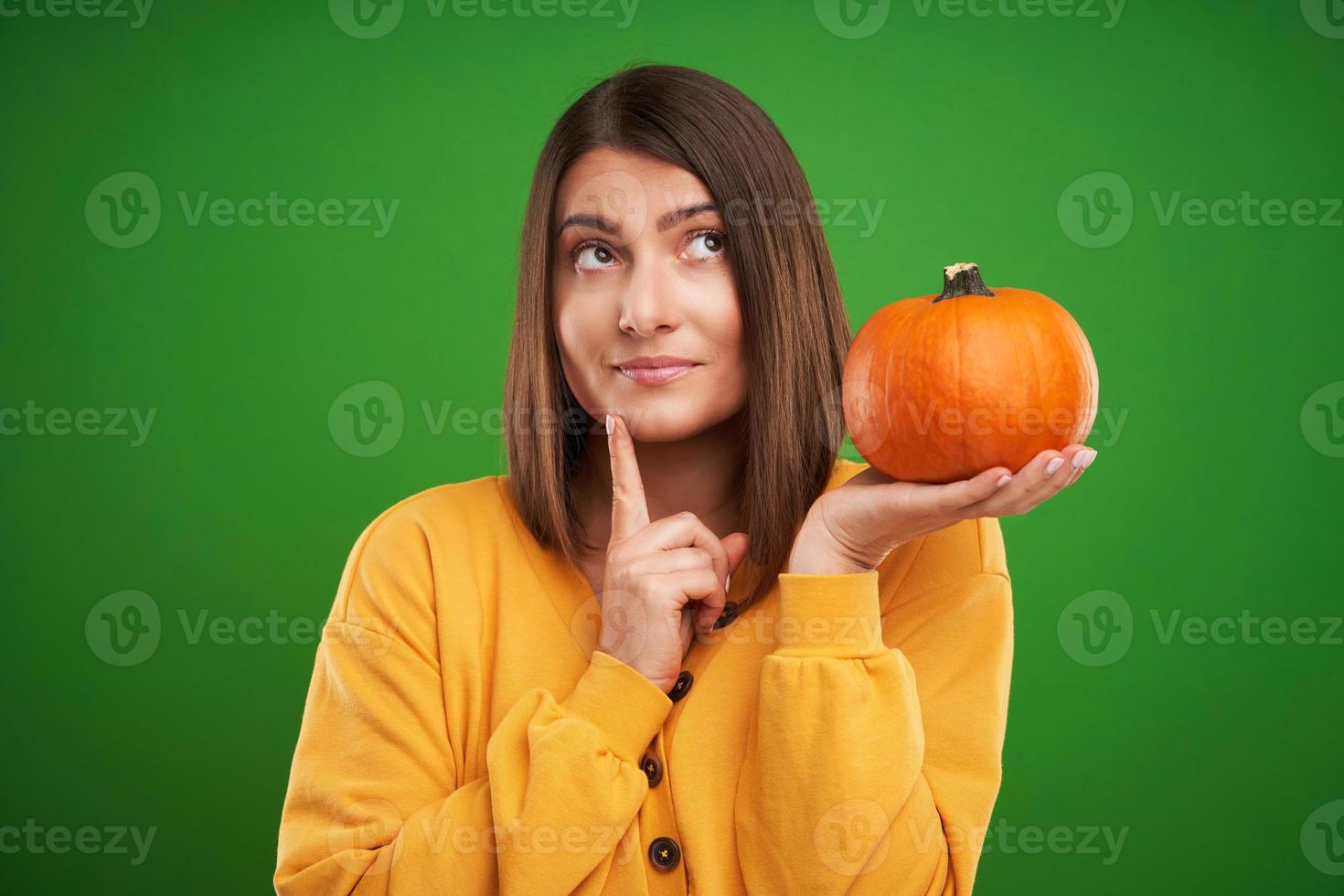 Close up of woman in yellow sweater holding pumpkin over green background photo