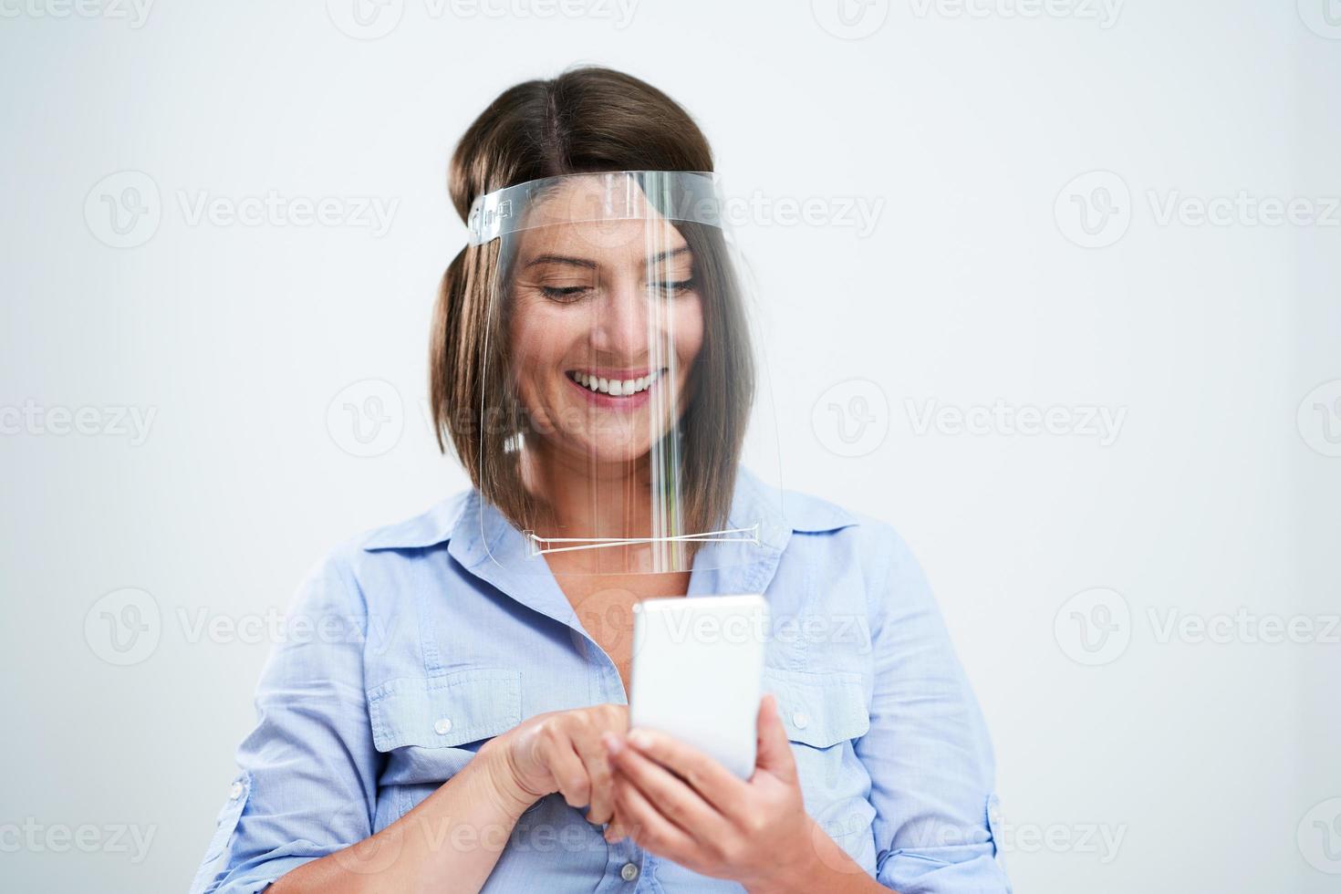 Woman wearing protective mask holding smartphone over white background photo
