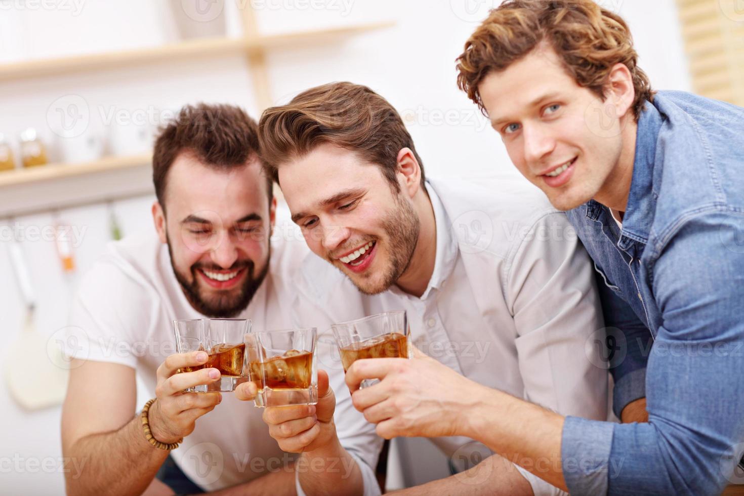 Cheerful friends having fun with smartphone and drinking at home photo