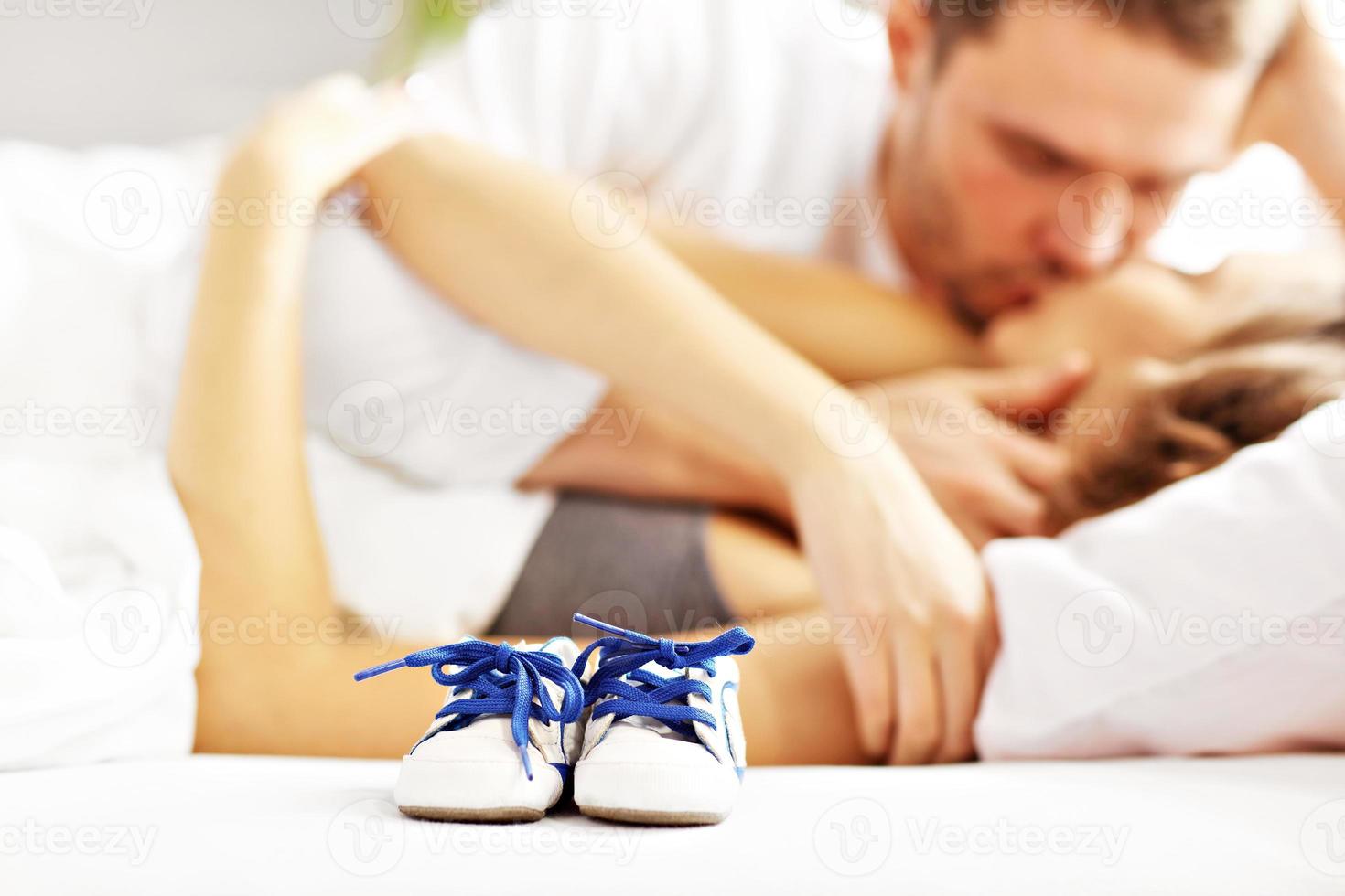 Happy couple kissing in bed and baby shoes photo