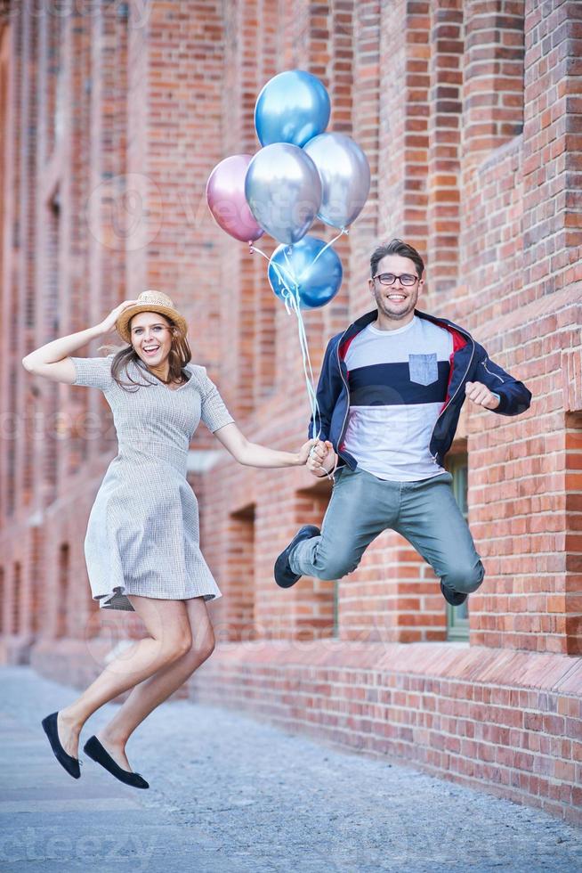 Adult couple holding balloons and jumping in the city photo