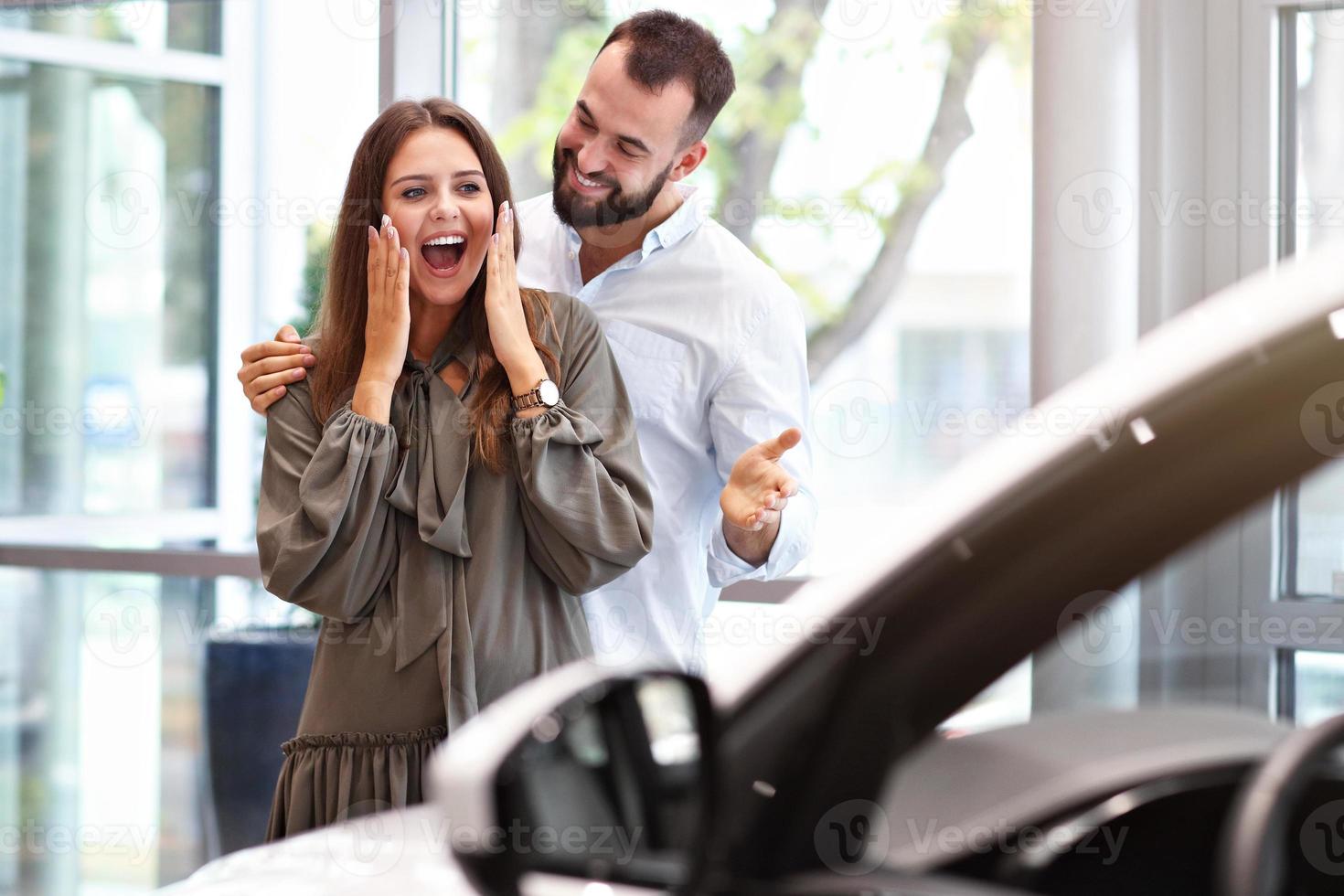 hombre adulto sorprendiendo a una mujer hermosa en la sala de exposición de automóviles foto