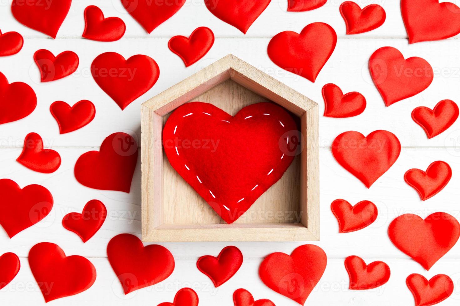primer plano de corazón rojo en una casa decorada con pequeños corazones sobre fondo de madera. día de San Valentín. concepto de hogar dulce hogar foto