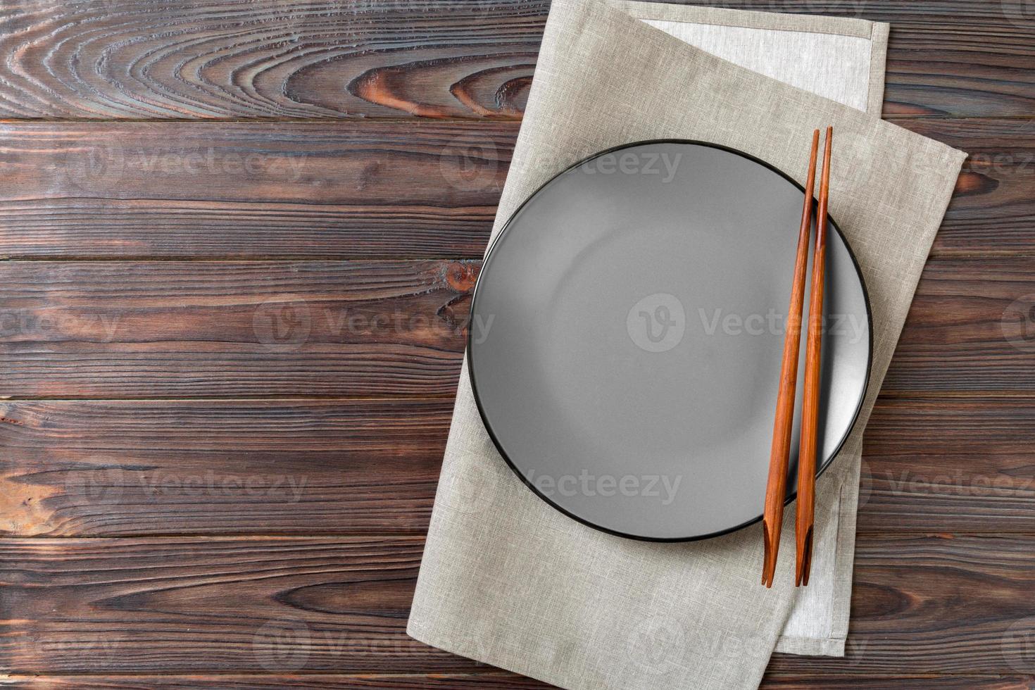Empty grey round plate with chopsticks for sushi and soy sauce on wooden background. Top view with copy space photo