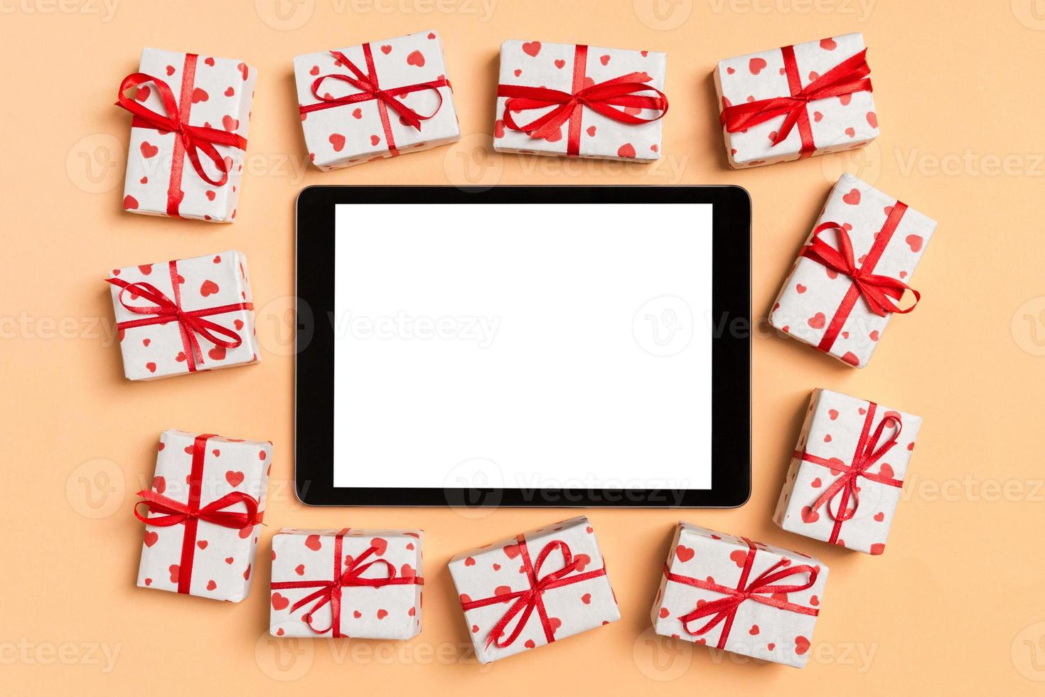 Top view of digital tablet surrounded with gift boxes on colorful background. Saint Valentine's day photo