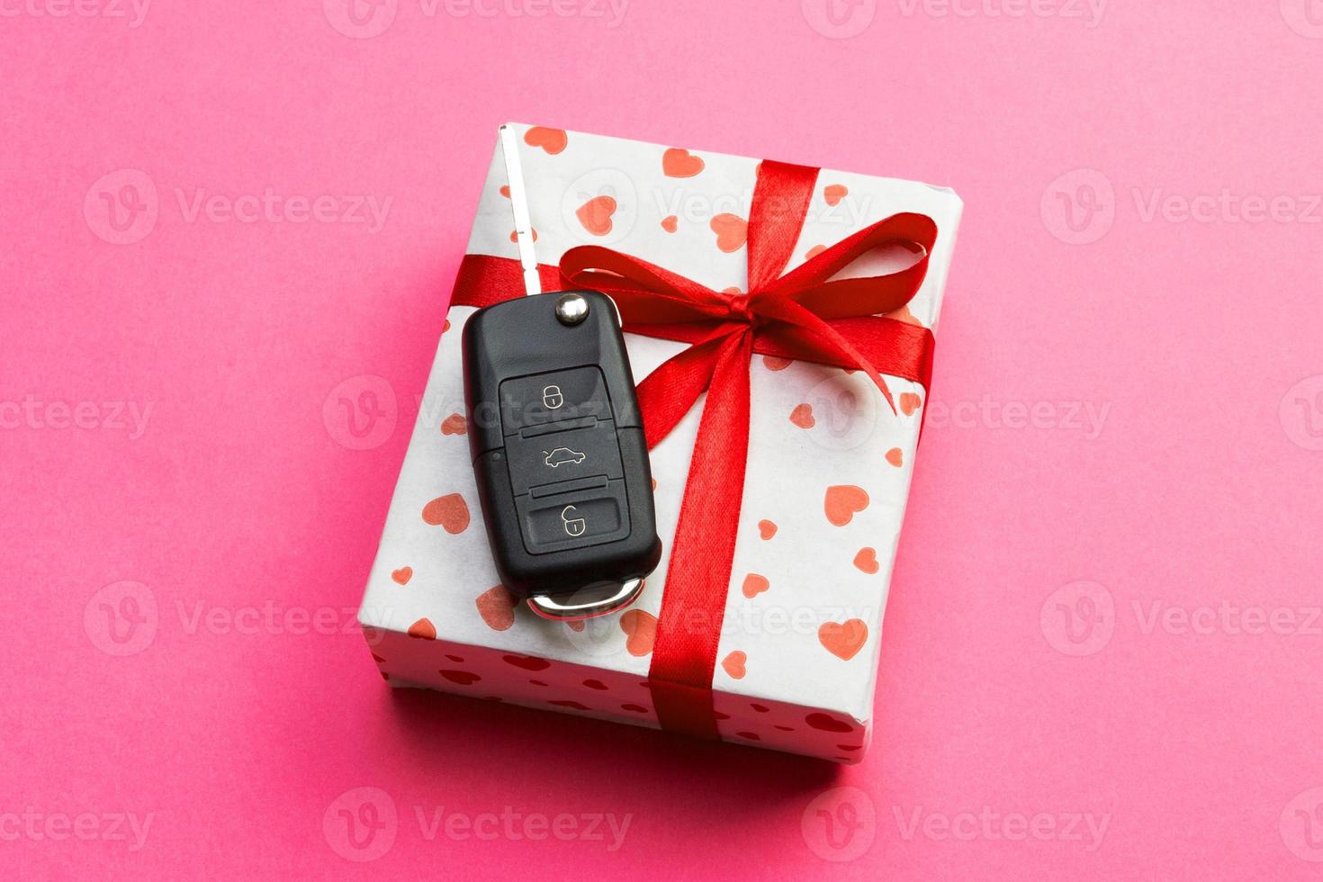 Car key on paper gift box with red ribbon bow and heart on pink table background. Holidays present top view concept photo