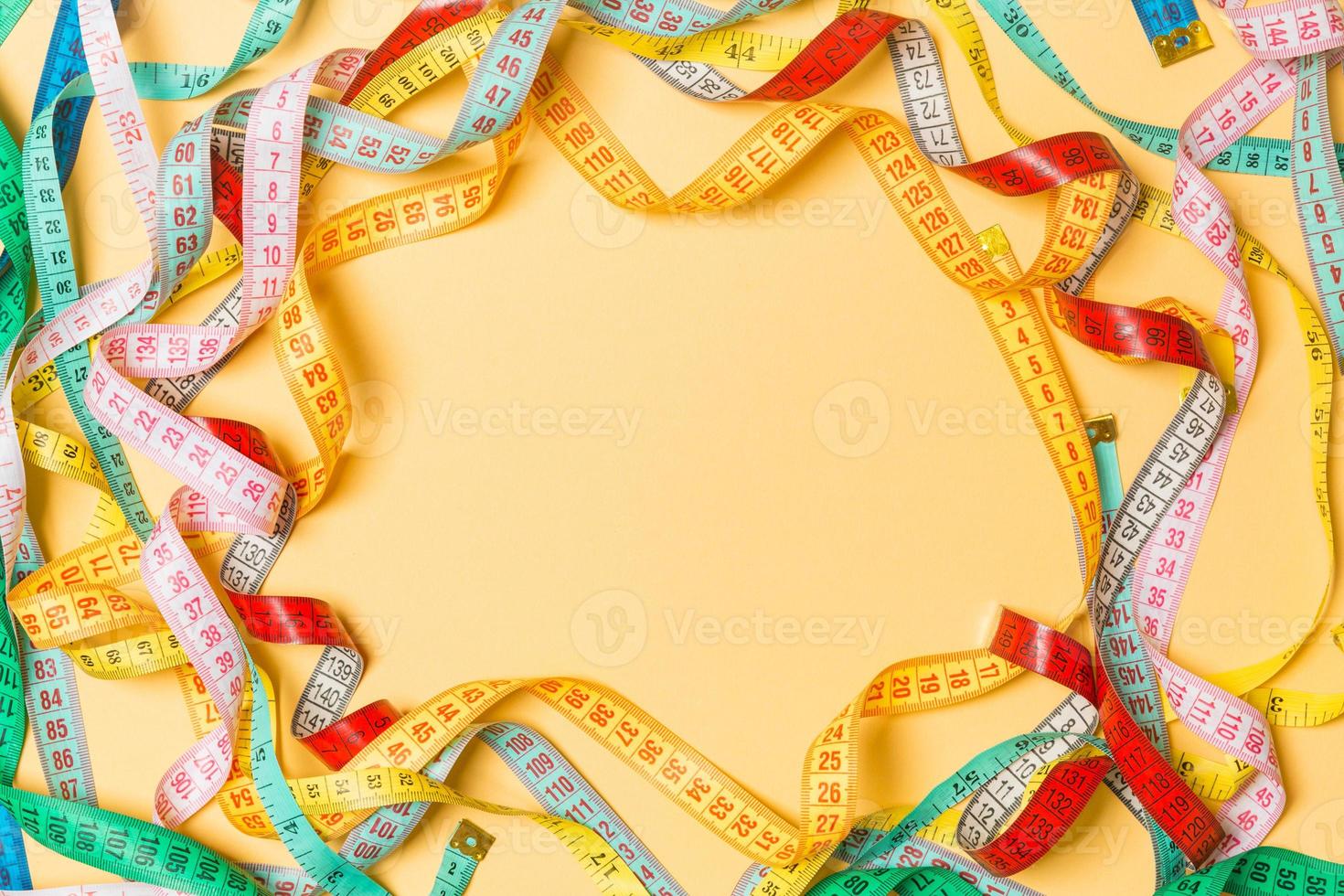 Heap of colorful measuring tapes in the form of frame on orange background. Top view of slim waist concept with copy space photo