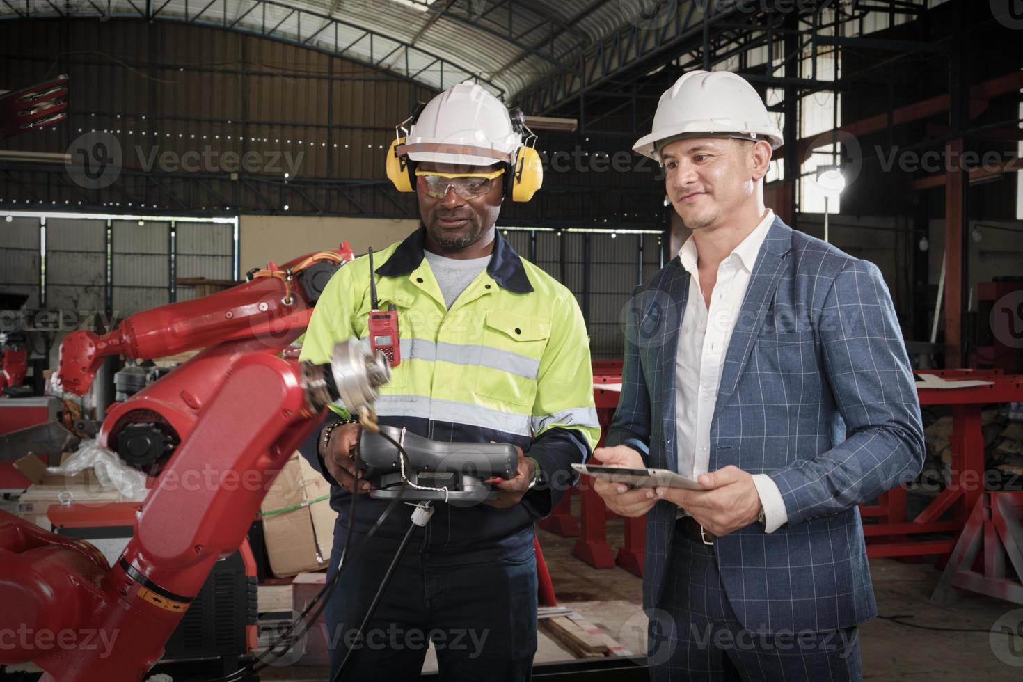 un ingeniero afroamericano demuestra un control de brazo robótico inteligente al cliente en una fábrica de fabricación mecánica, máquinas automáticas inteligentes en negocios industriales y tecnología futurista. foto