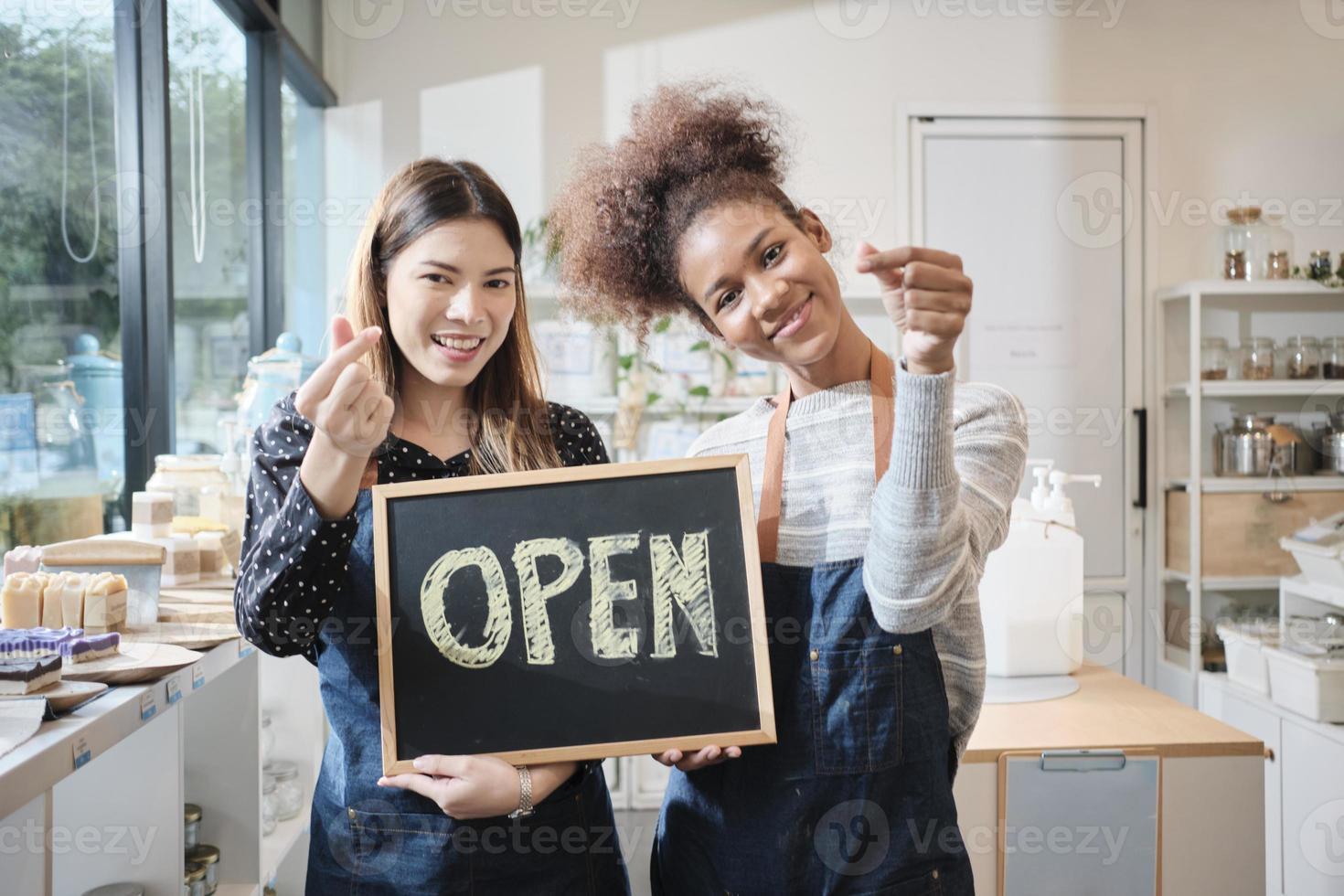 dos jóvenes comerciantes muestran un letrero abierto con sonrisas alegres en la tienda de recarga, trabajo feliz con productos orgánicos, comestibles sin desperdicio, mercadería ecológica y negocios sostenibles. foto