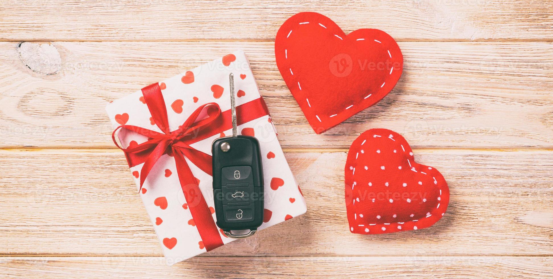 Valentine or other holiday handmade present in paper with red hearts, car keys and gifts box in holiday wrapper. box gift on orange wooden table top view with copy space, empty space for design photo