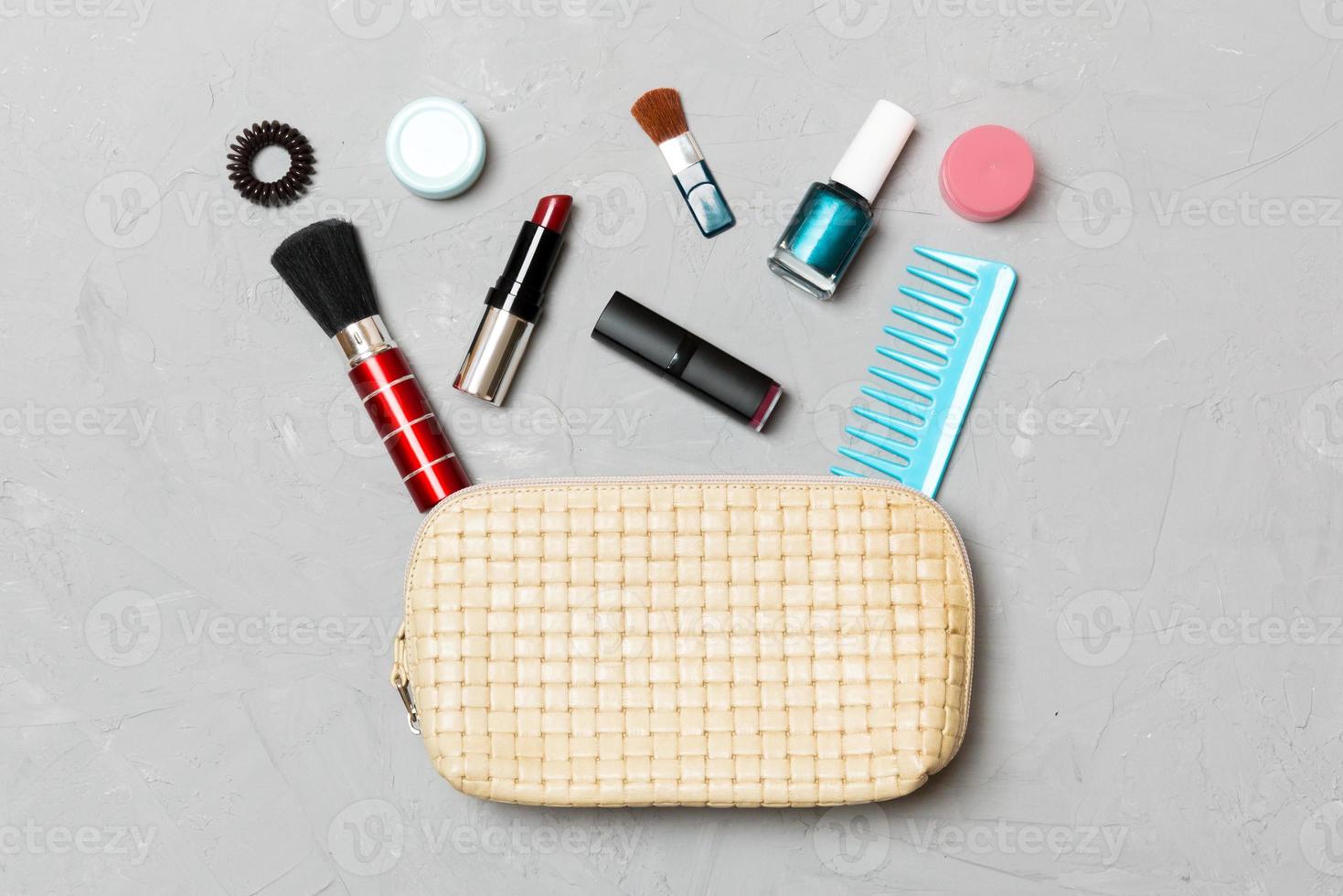 Top view of set of make up and skin care products spilling out of cosmetics bag on cement background. Beauty concept photo