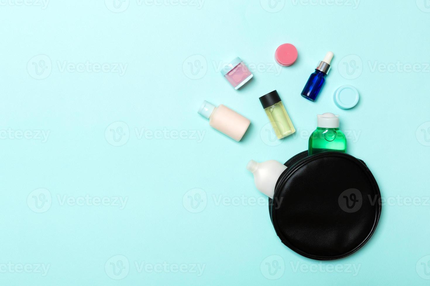 un grupo de botellas de crema de belleza se cayó de la bolsa de cosméticos con fondo azul. espacio para su diseño. vista superior del concepto de cuidado de la piel foto