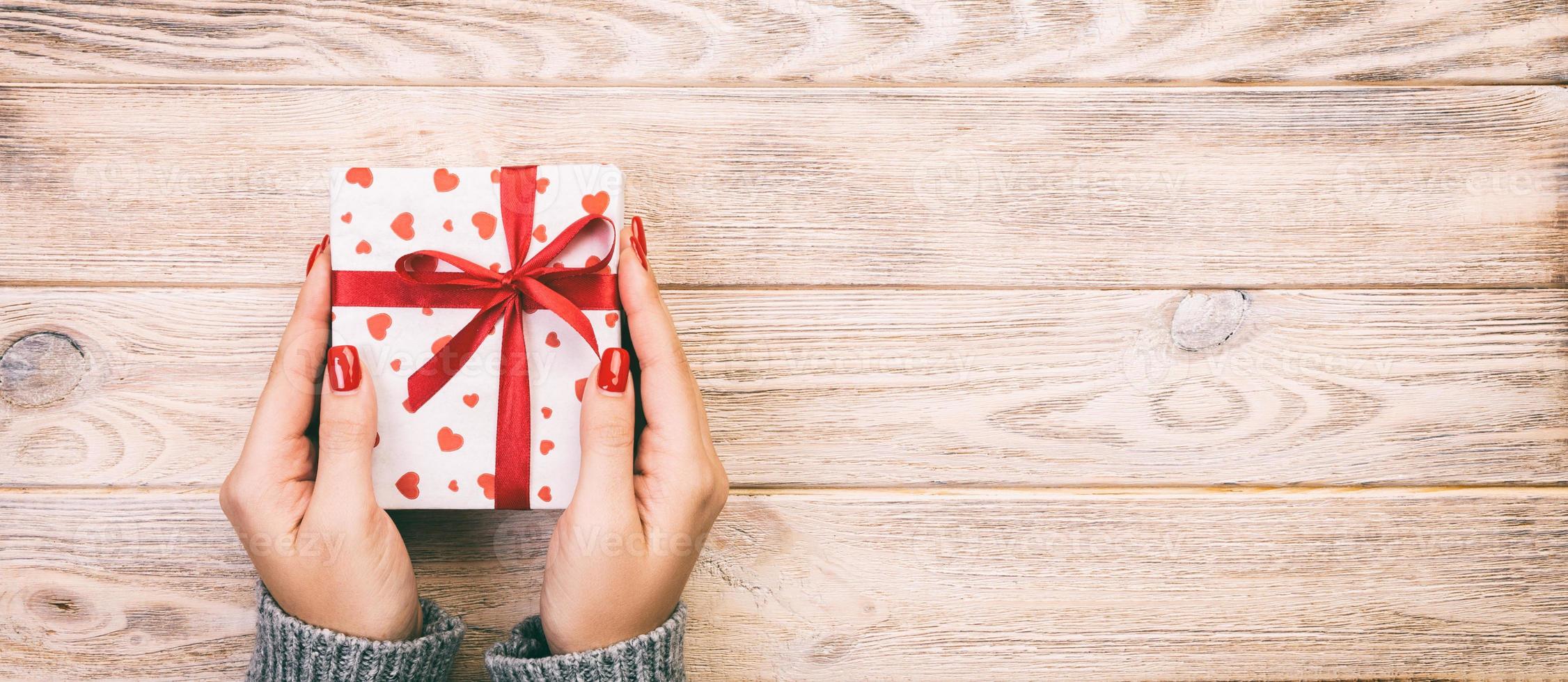 Woman hands giving Holidays gift box on wood table, Present box, red heart decoration of gift on wooden table, top view with copy space for you design. Toned web banner photo