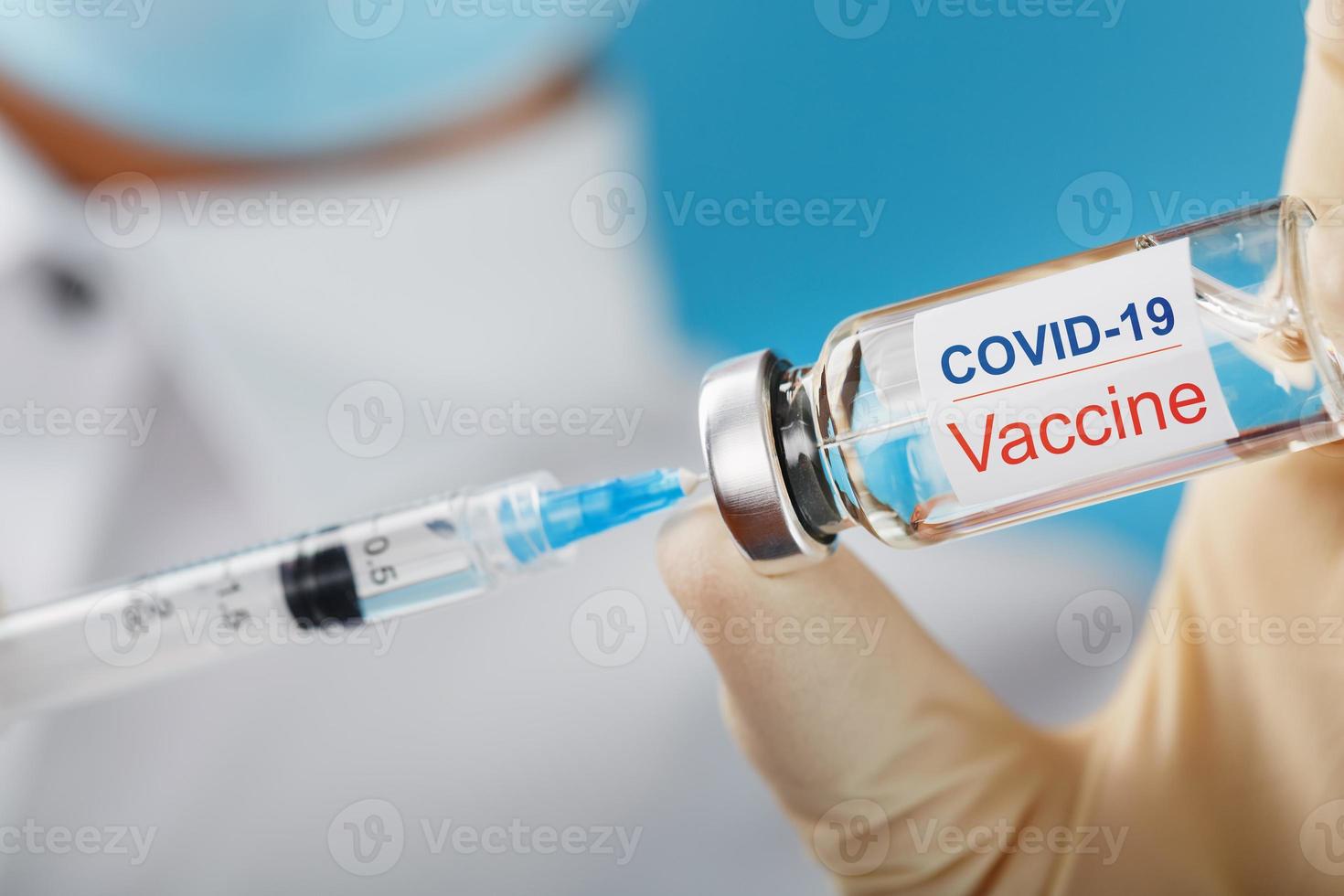 Syringe and ampoule with the inscription COVID-19 vaccine in the hands of a doctor-researcher in rubber gloves with a vaccine close-up. photo