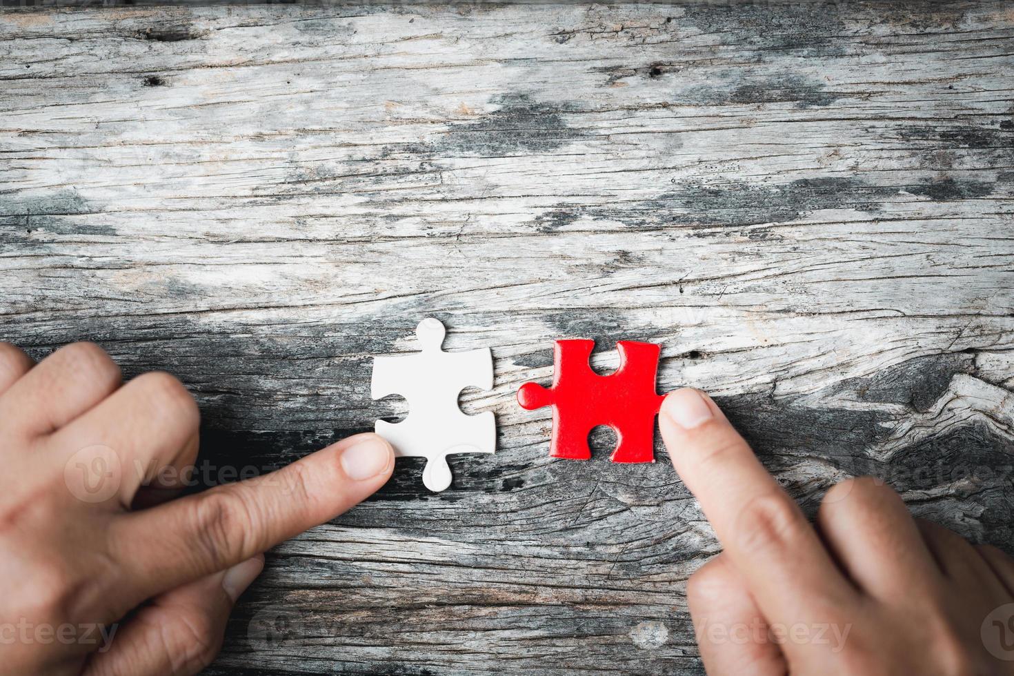Pieces of jigsaw puzzle in woman's hands. White details of jigsaw puzzle piece on wooden background. Concept of working together as a business team. The idea of getting involved, working for success. photo