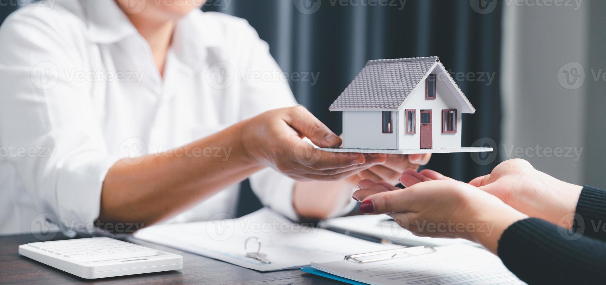 Real estate agents offer contracts to purchase or rent residential. Business person hands holding home model, small building red house. Mortgage property insurance moving home and real estate concept photo