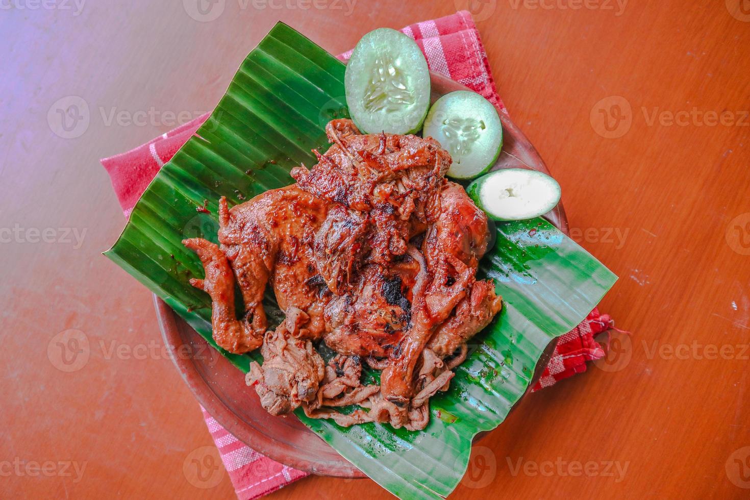 grilled chicken or ayam bakar with cucumber slash served on banana leaf and plate. ayam bakar is traditional grilled chicken from indonesia photo