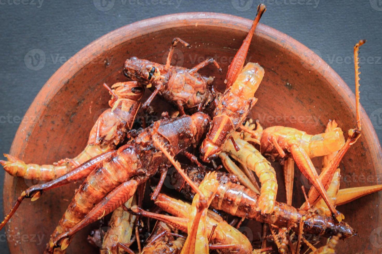 fried grasshopper or belalang goreng is traditional food from southeast asia, served with sambal, onion, garlic, chili on wood background photo