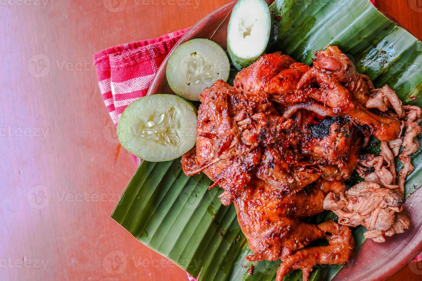 grilled chicken or ayam bakar with cucumber slash served on banana leaf and plate. ayam bakar is traditional grilled chicken from indonesia photo