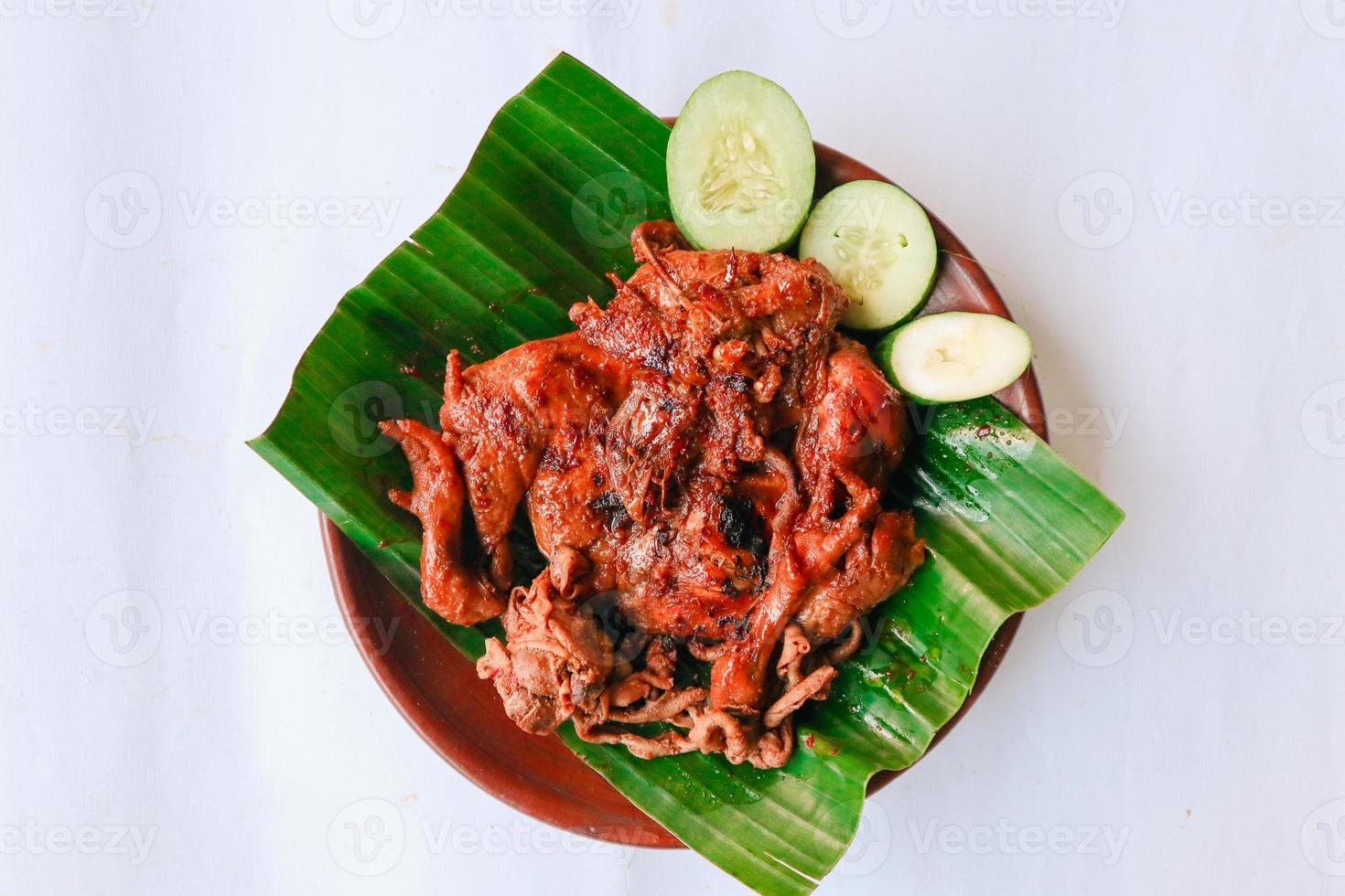 grilled chicken or ayam bakar with cucumber slash served on banana leaf and plate. ayam bakar is traditional grilled chicken from indonesia photo