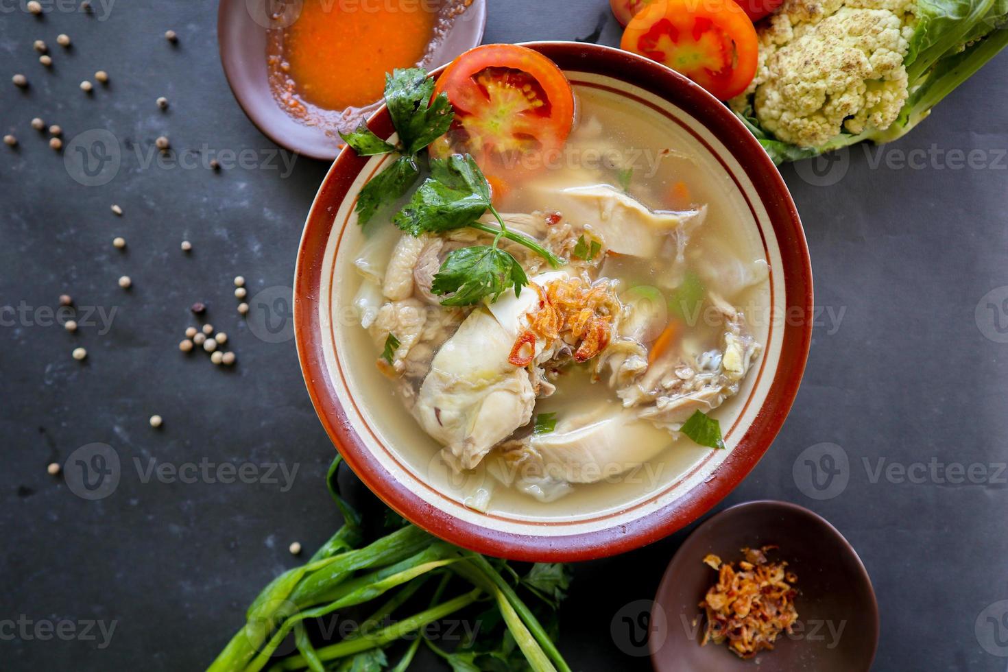 Chicken soup served with vegetables, tomatoes, celery in a bowl, spoon and fork. with black background photo