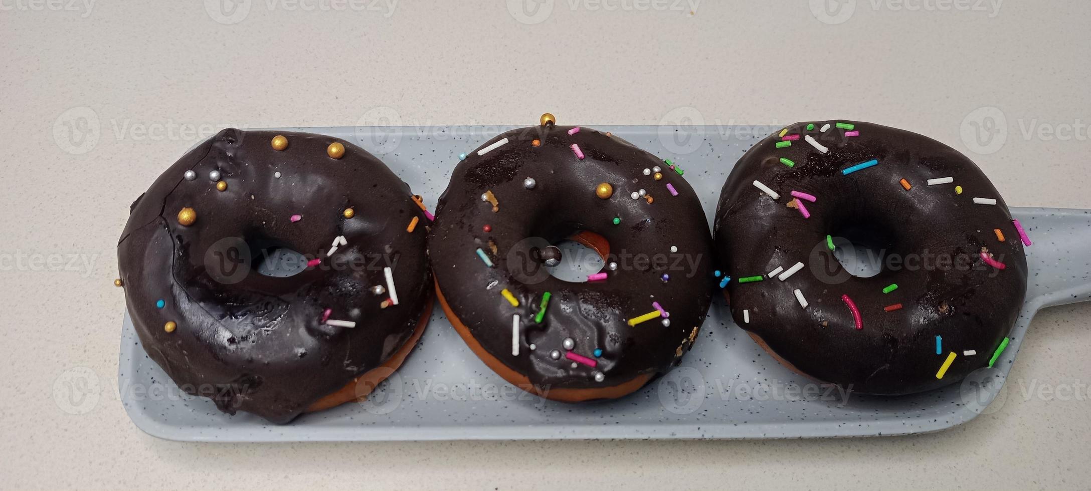 assorted donuts with chocolate frosted, pink glazed and sprinkles donuts. Donuts in hand or tray photo