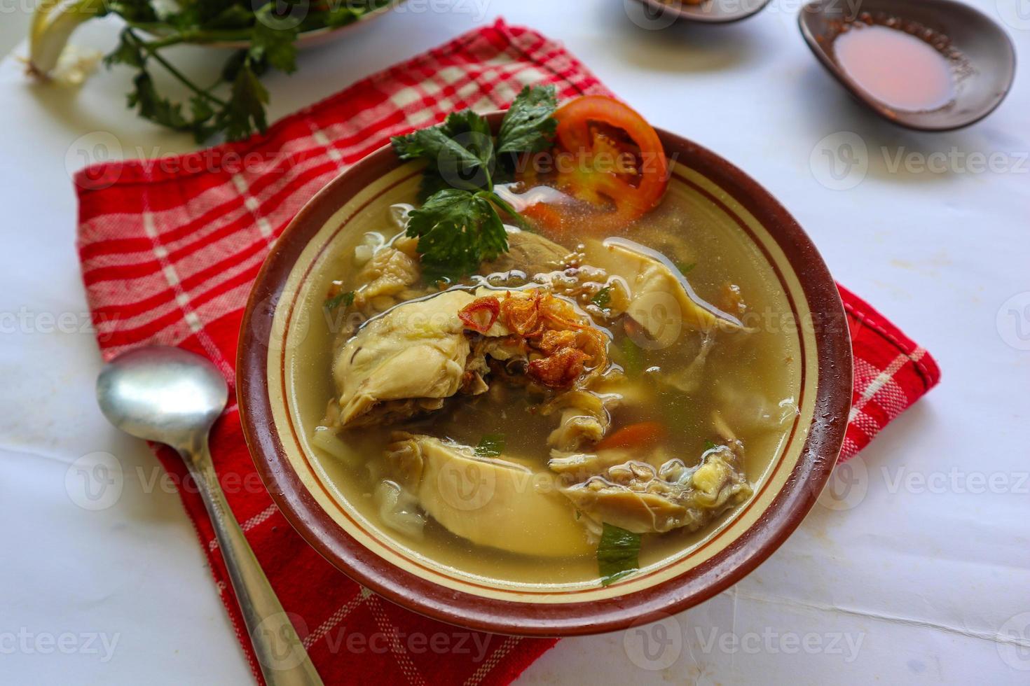 Chicken soup served with vegetables, tomatoes, celery in a bowl, spoon and fork. with black background photo