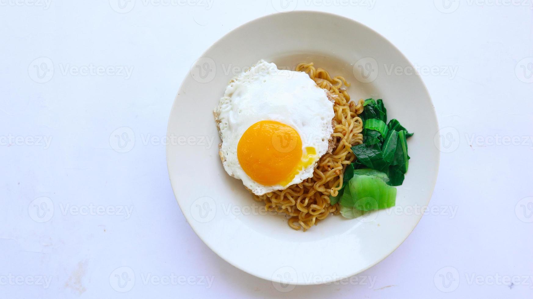 instant noodles served with egg fried and mustard greens on plate. instant fried noodle indomie photo