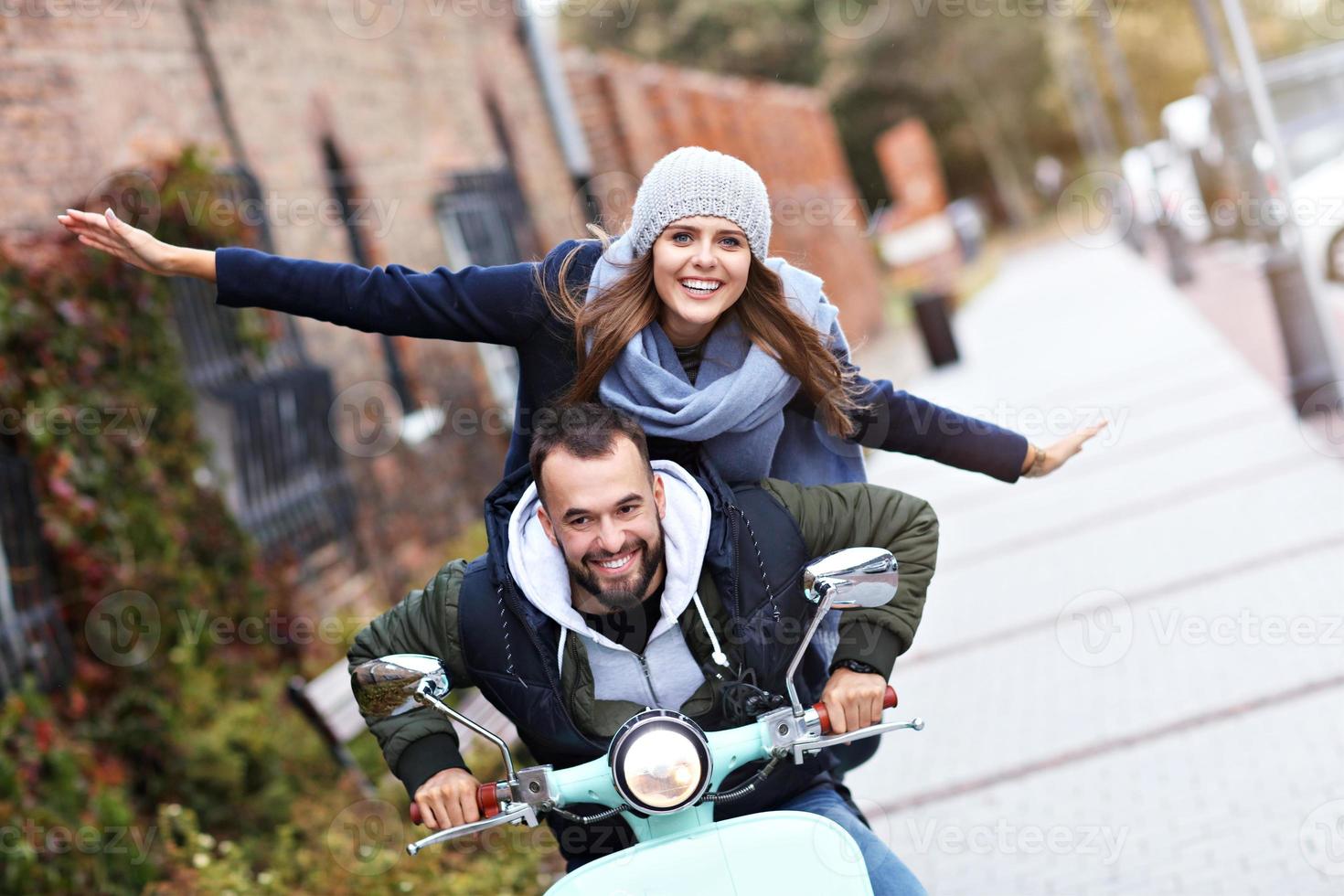 Beautiful young couple smiling while riding scooter in city in autumn photo