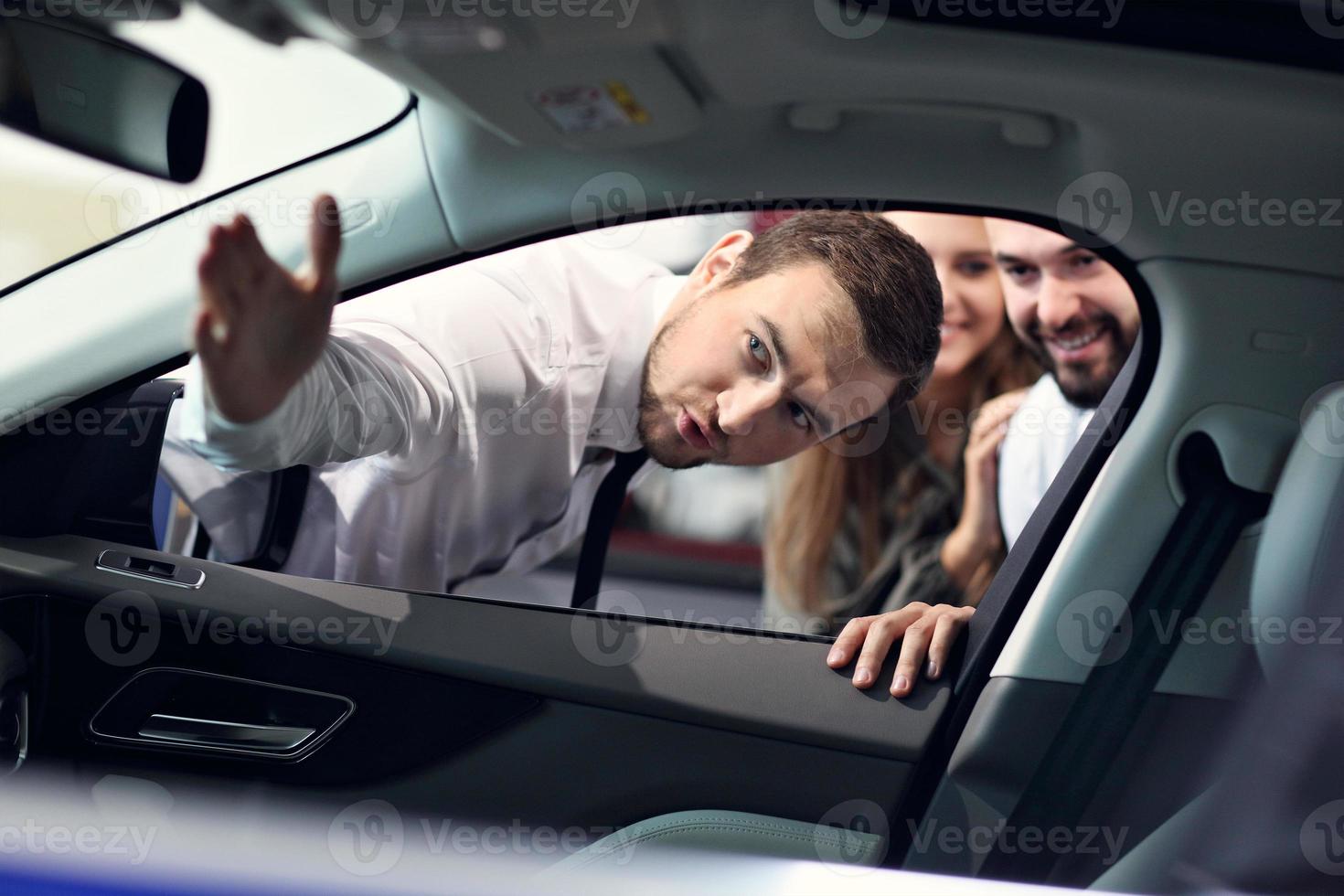 vendedor joven confiado que explica las características del coche a los dueños atractivos jóvenes foto