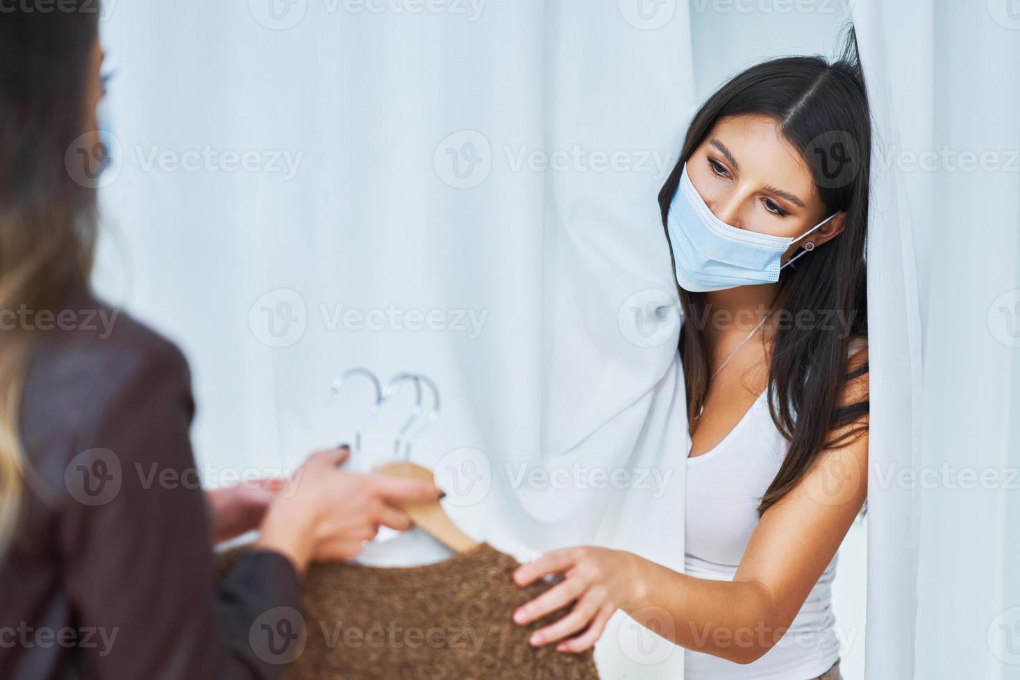 Two girl friends in clothes store in changing room in mask photo