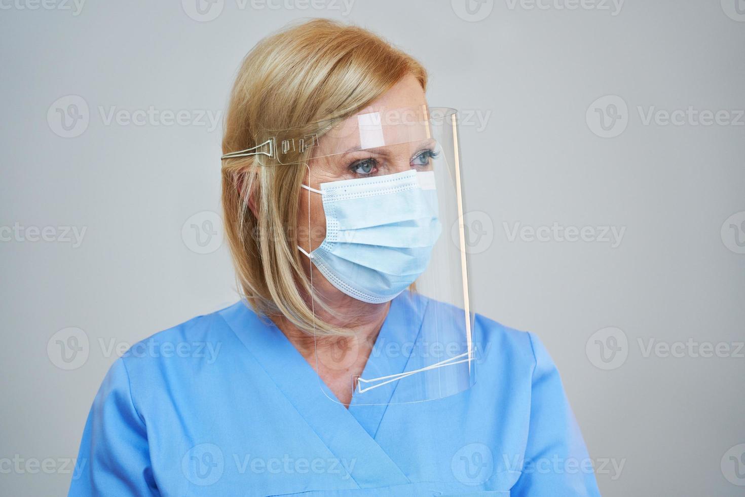 Senior female doctor posing in mask and shield over gray background photo