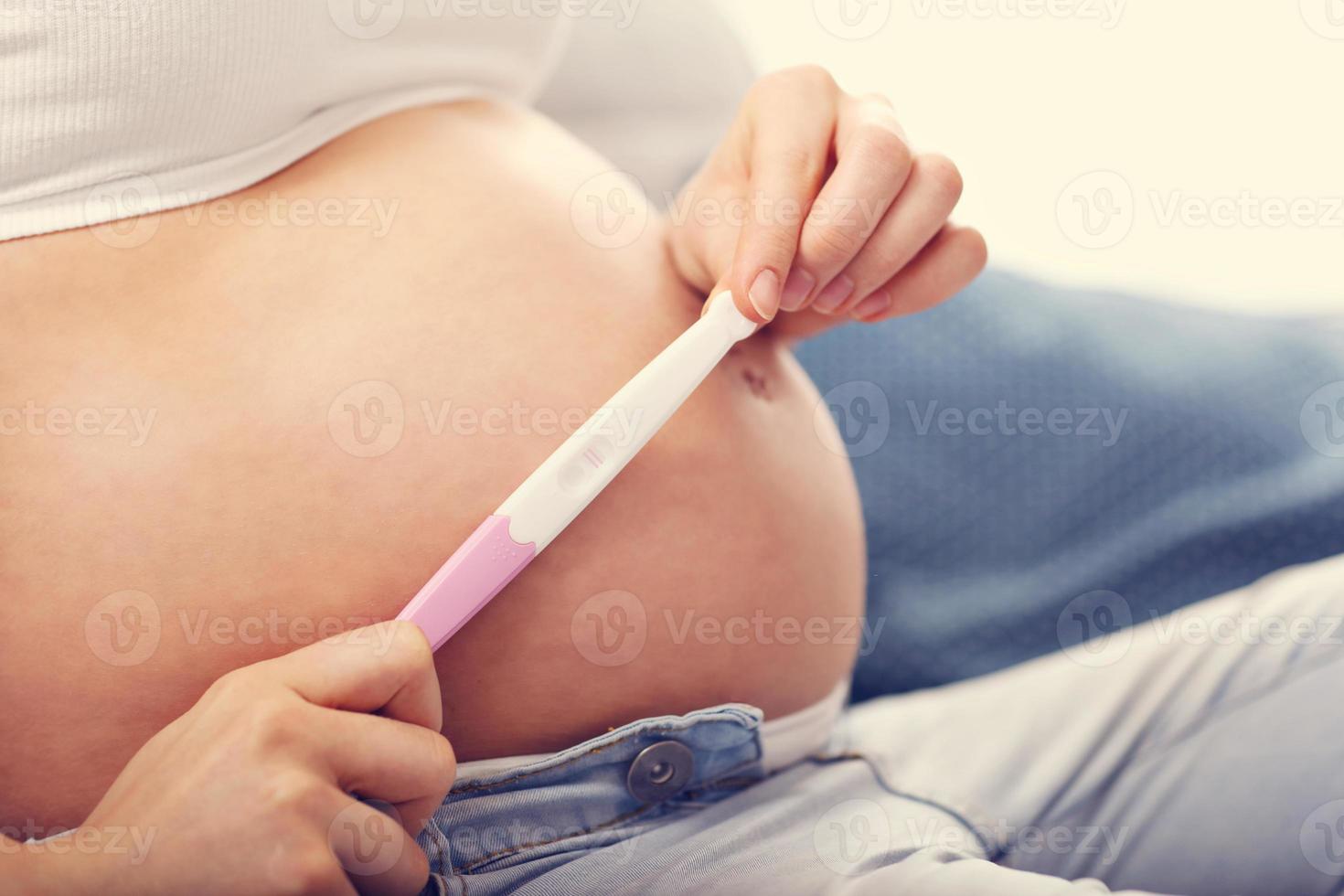 Happy pregnant woman resting on sofa with pregnancy test photo