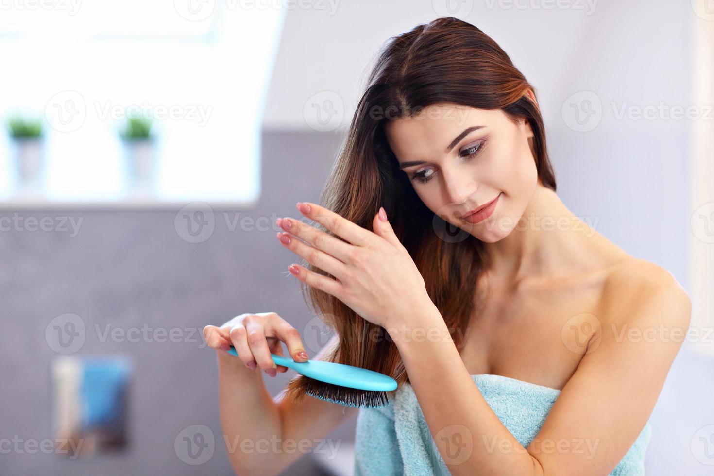mujer joven de pie en el baño y cepillando el cabello foto