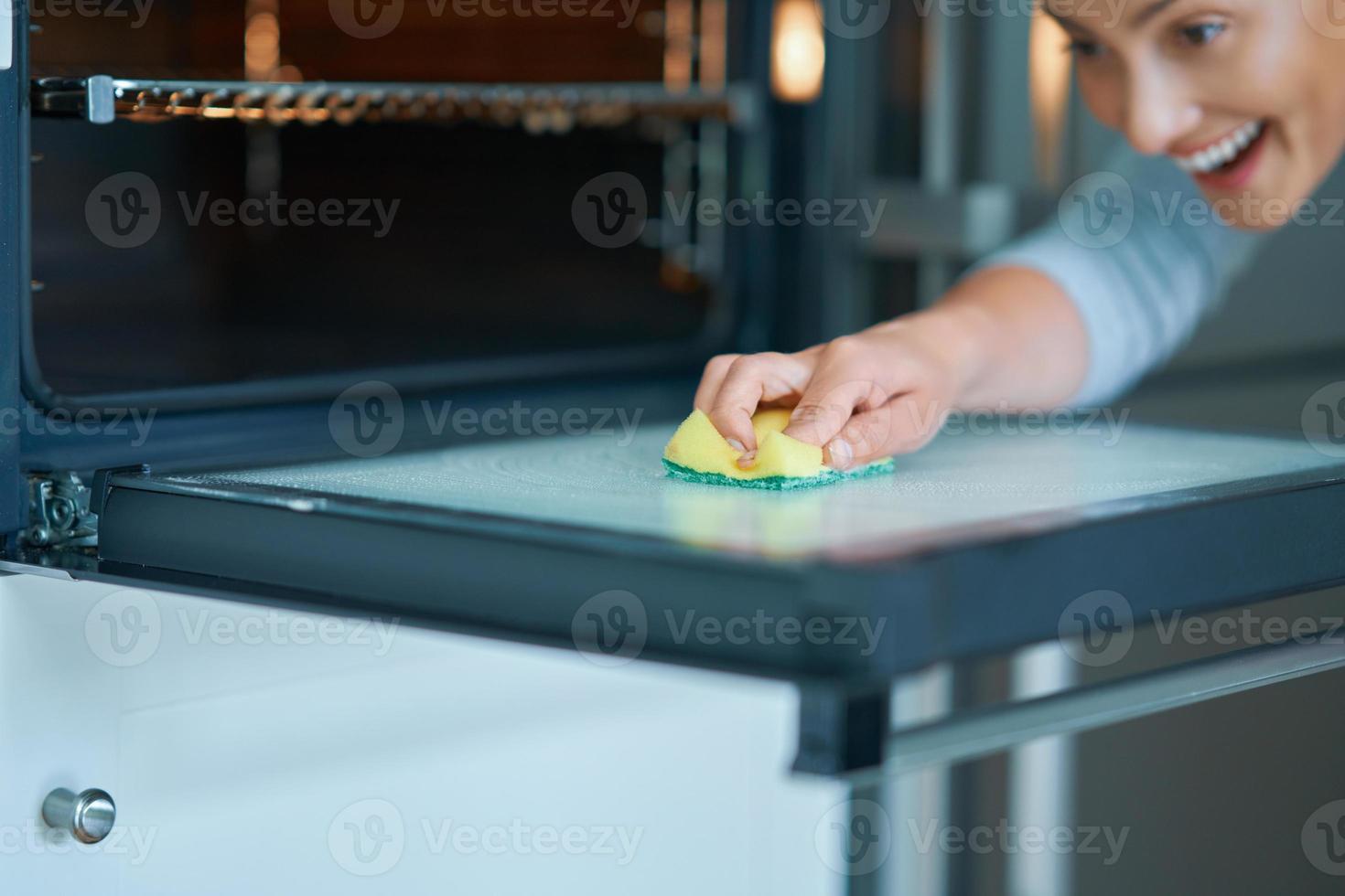 mujer joven limpiando el horno en la cocina foto