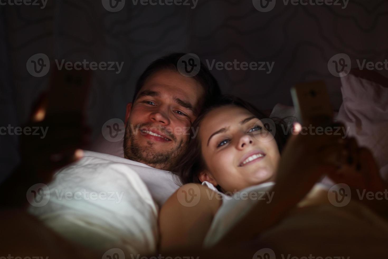 pareja joven usando teléfonos inteligentes en la cama por la noche foto
