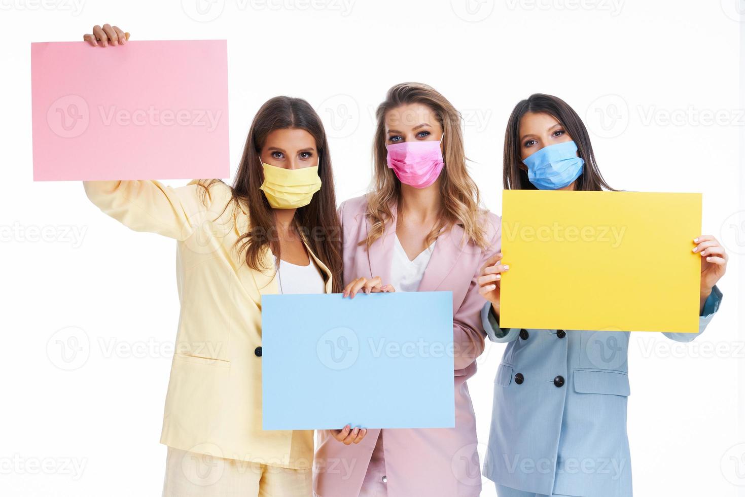 Three women in pastel suits holding billboard posing over white background photo