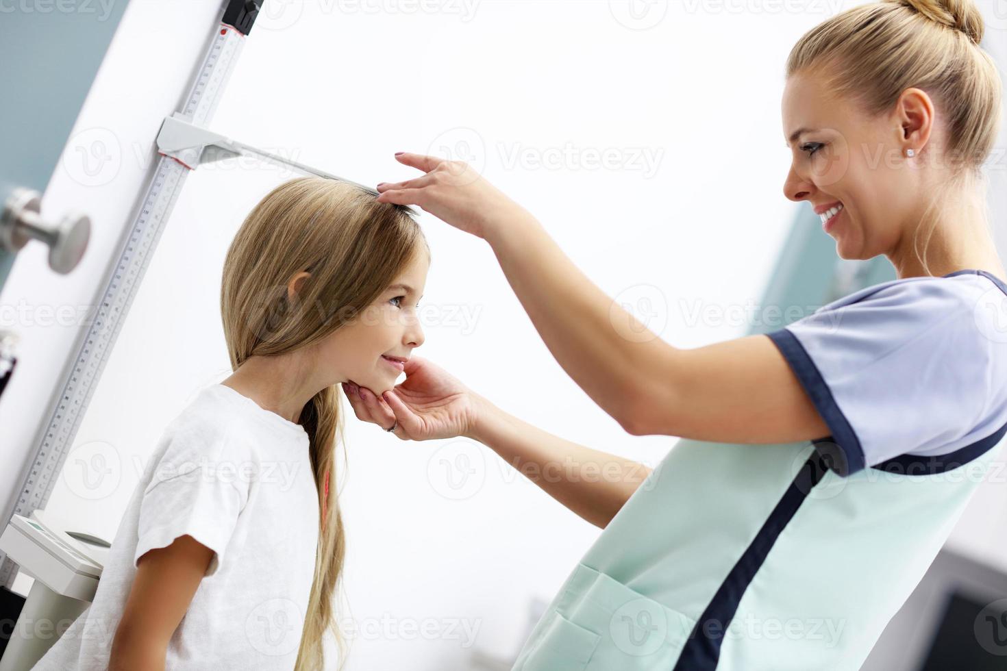 Female doctor measuring height of girl in clinic photo