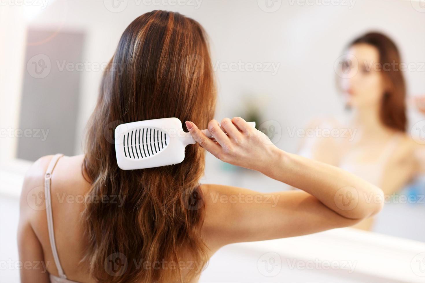 mujer joven de pie en el baño y cepillando el cabello foto