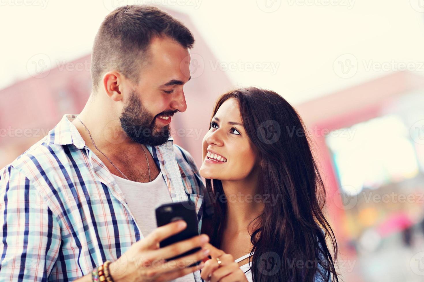 Happy couple using smartphone in city in rainy day photo