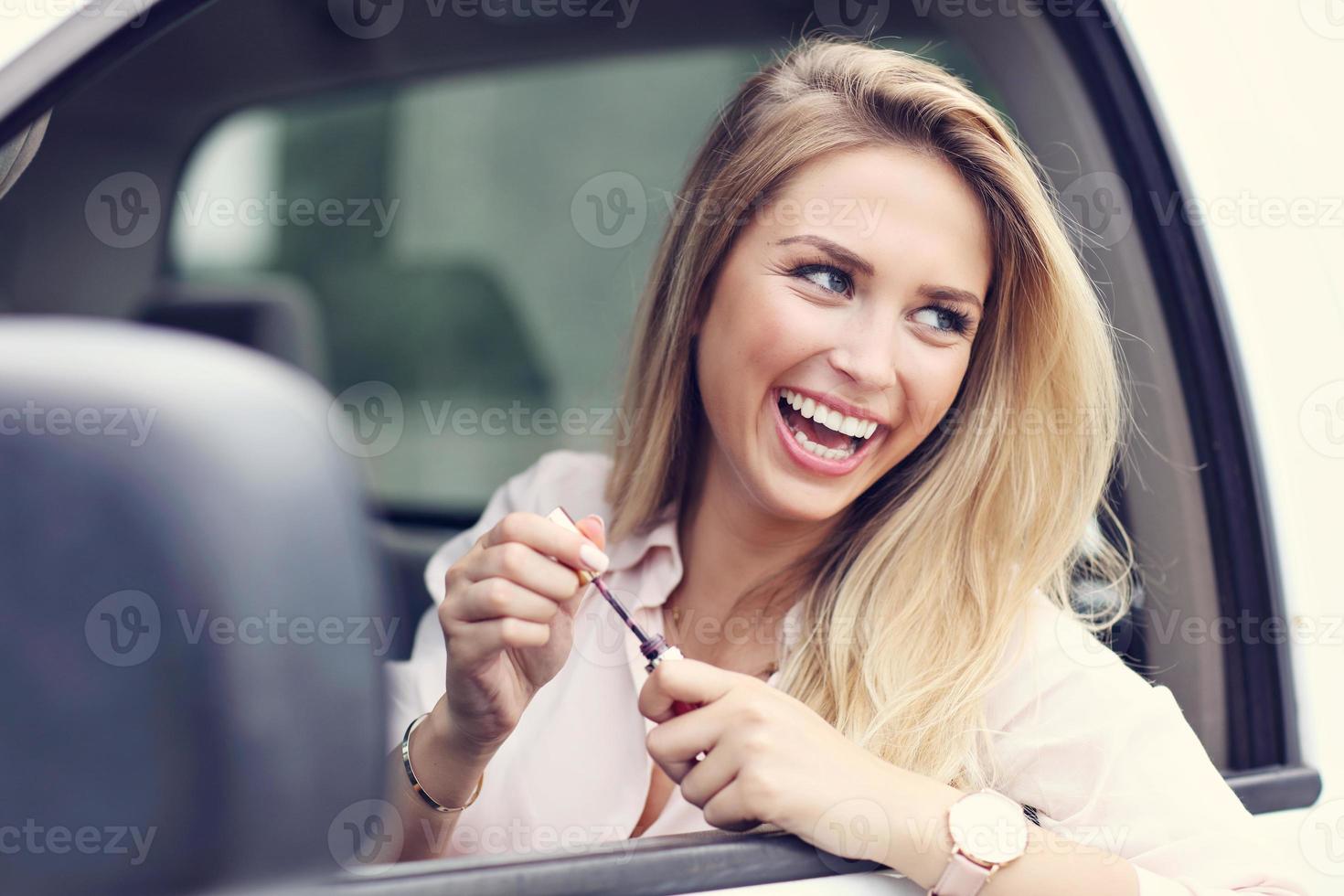 Young attractive woman looking in rear view mirror applying lipstick photo