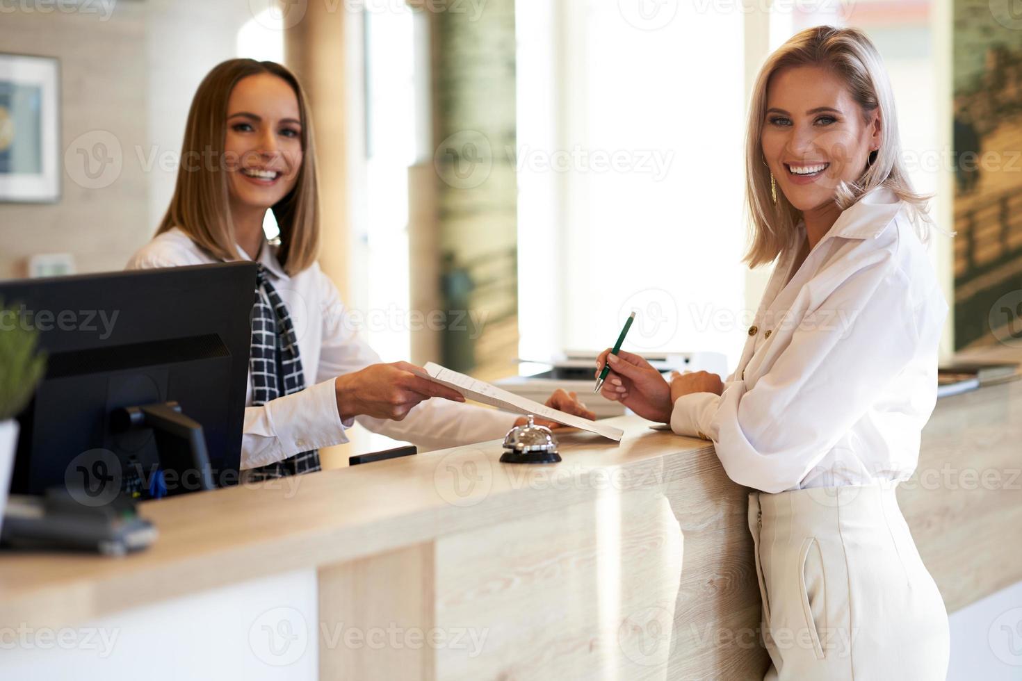 Receptionist and businesswoman at hotel front desk photo