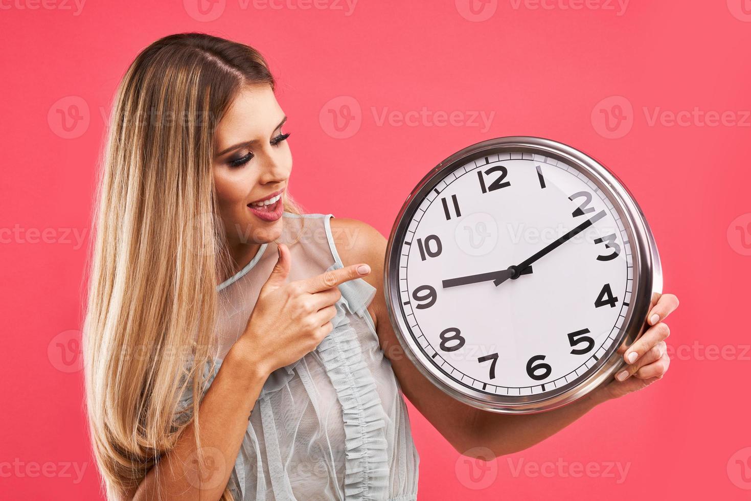 Beautiful adult woman posing over pink background with clock photo