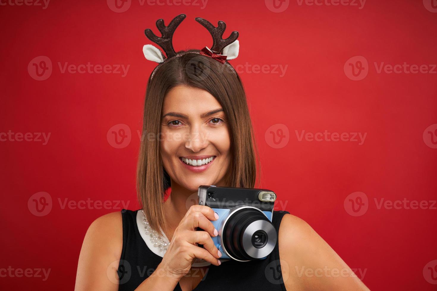 Adult happy woman in Christmas mood taking instant pictures over red background photo