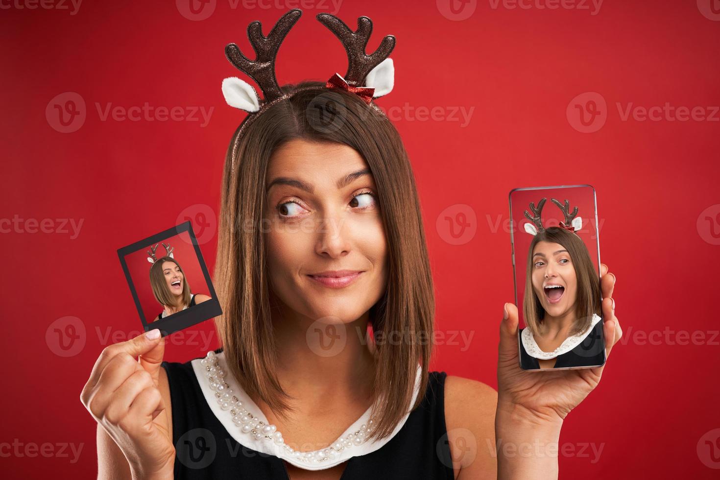 Woman in Christmas mood comparing instant pictures to smartphone camera over red photo