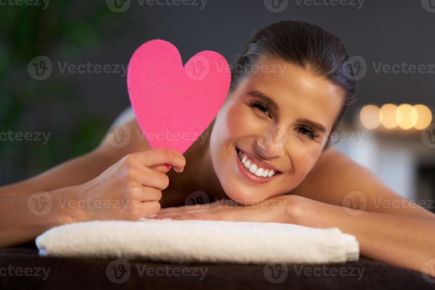 Relaxed woman waiting for a back massage and holding heart photo